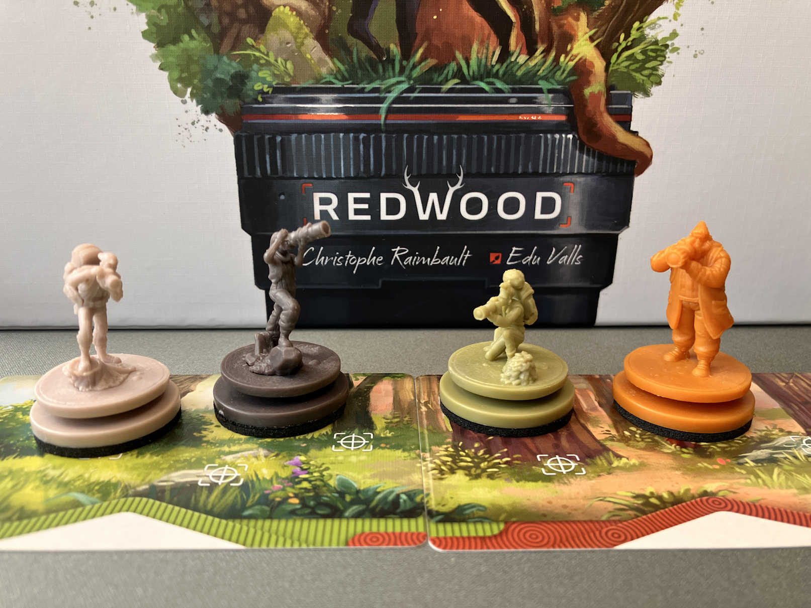 Die 4 Miniaturen in spielerfarben vor der Spielschachtel